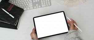 Top view of female graphic designer using tablet with colour swatches on white table.