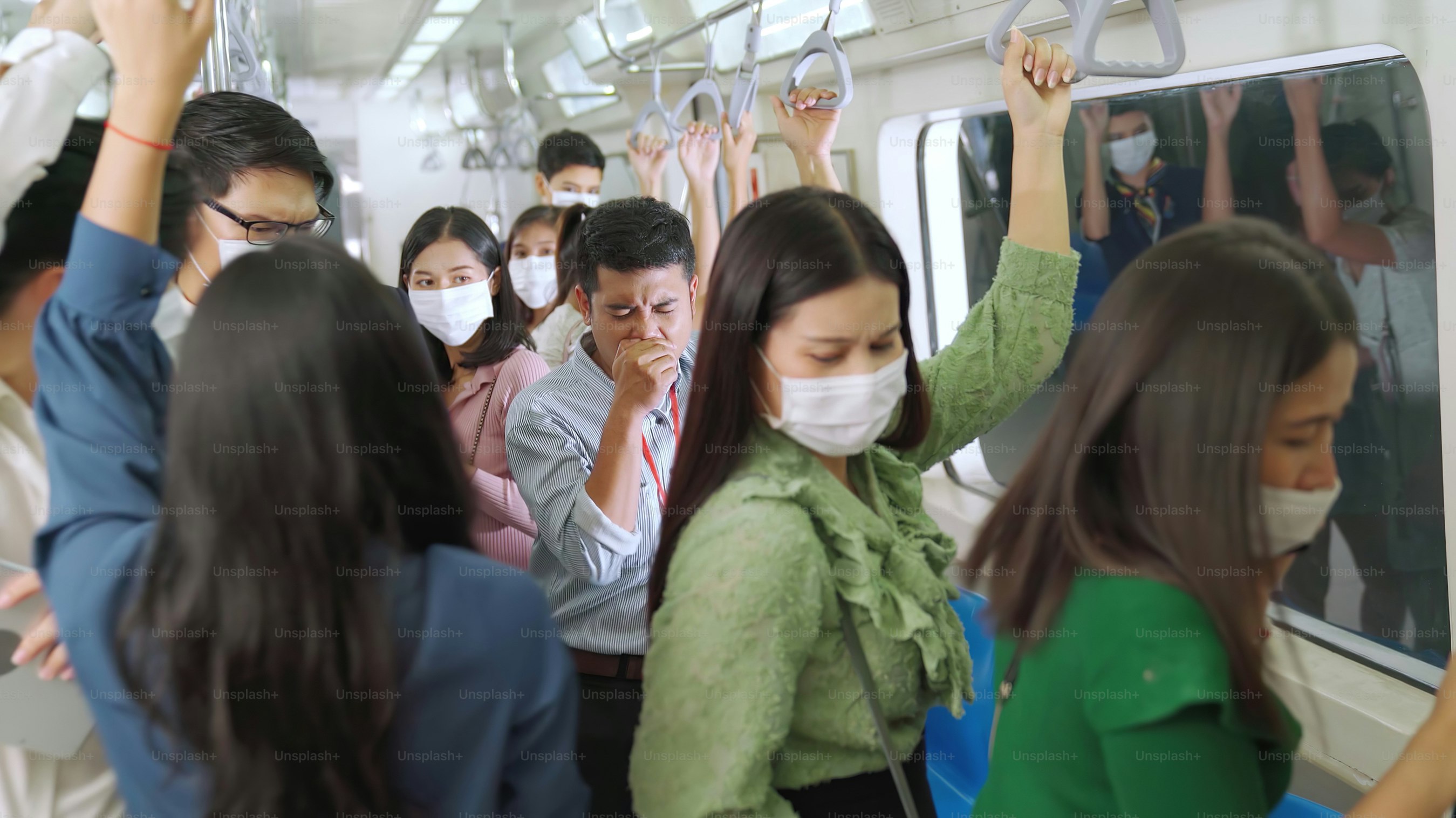 Commuters wearing face masks holding overhead straps inside a crowded subway train
