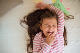 Top view portrait of unhappy small girl lying on bed indoors, crying.