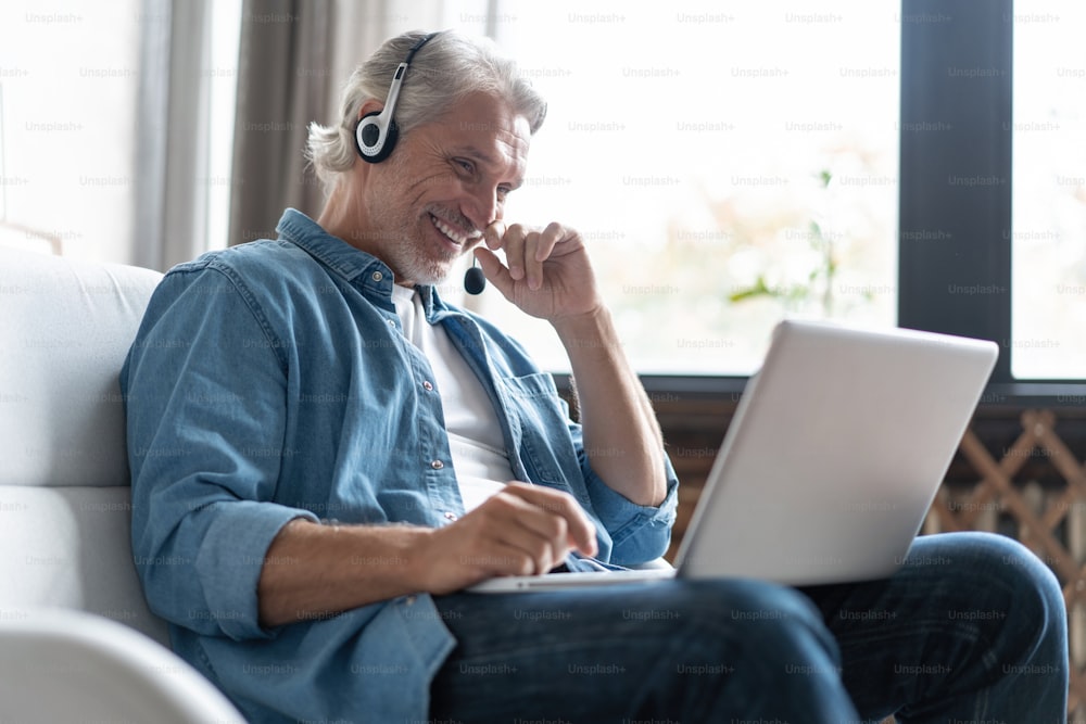 Smiling man in headset watch webinar or training on modern computer, male call center agent or telemarketer work consult client online