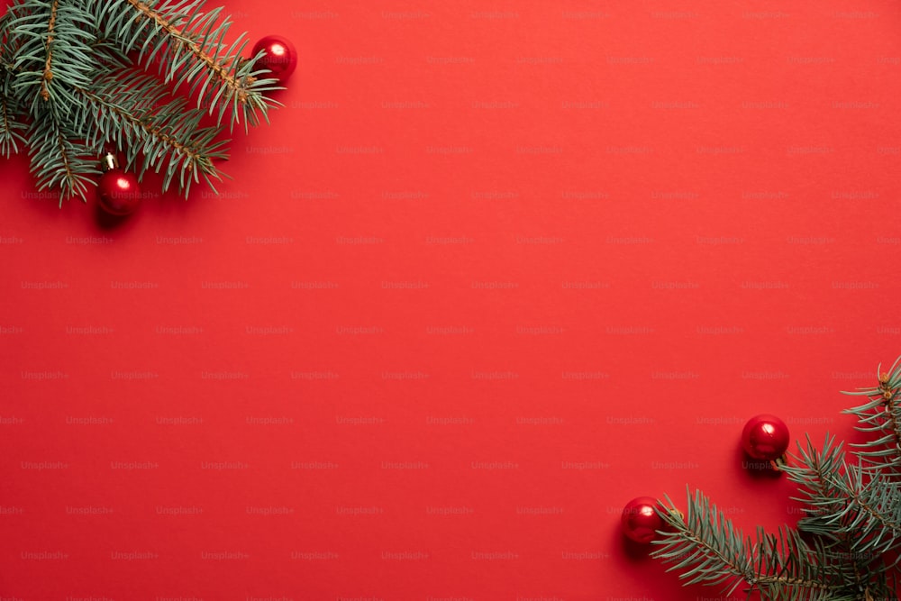 Christmas tree branches and red balls decoration on red background. Christmas greeting card, frame, banner mockup. Flat lay, top view, copy space.