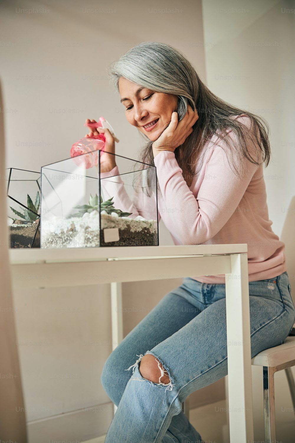 Beautiful lady holding water spray bottle and smiling while sitting at the table with geometric glass succulent terrariums