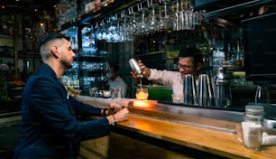 Caucasian man sitting at bar counter waiting cocktail drink from barman in nightclub.