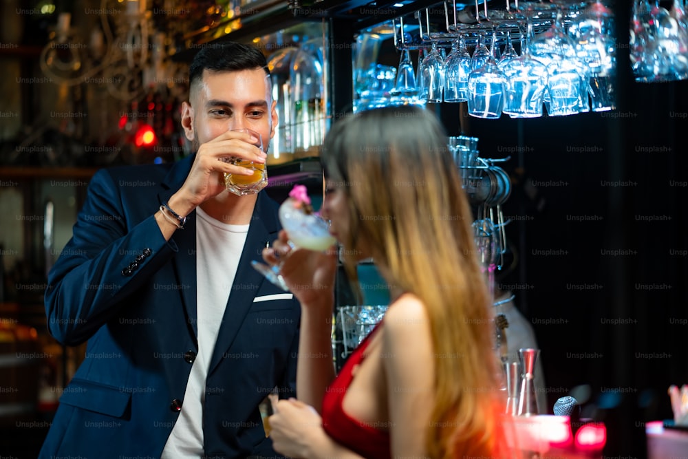 Retrato do homem caucasiano falando com a bela mulher asiática com bebida de coquetel no bar