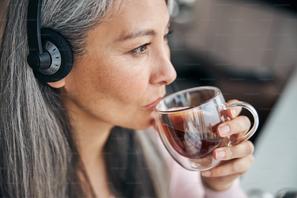 Gros plan d’une femme charmante sirotant sa boisson chaude préférée et détournant le regard avec une expression sereine