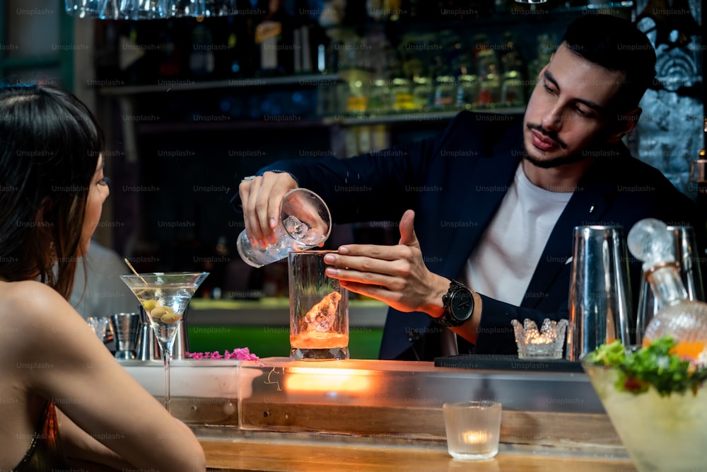 Männlicher Barkeeper gießt alkoholisches Getränk an weibliche Kundin