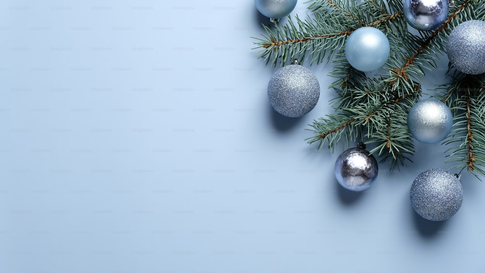 Elégante composition de Noël avec décoration boules bleues et argentées et branche de pin sur fond bleu pastel. Pose à plat, vue de dessus.