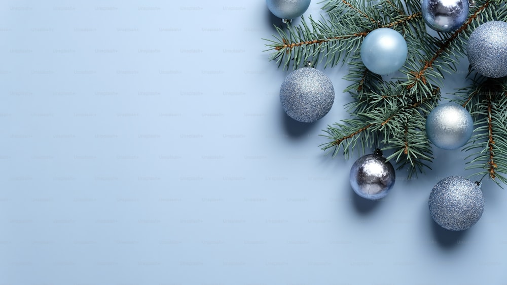 Elegante composición navideña con decoración de bolas azules y plateadas y rama de pino sobre fondo azul pastel. Plano, vista superior.