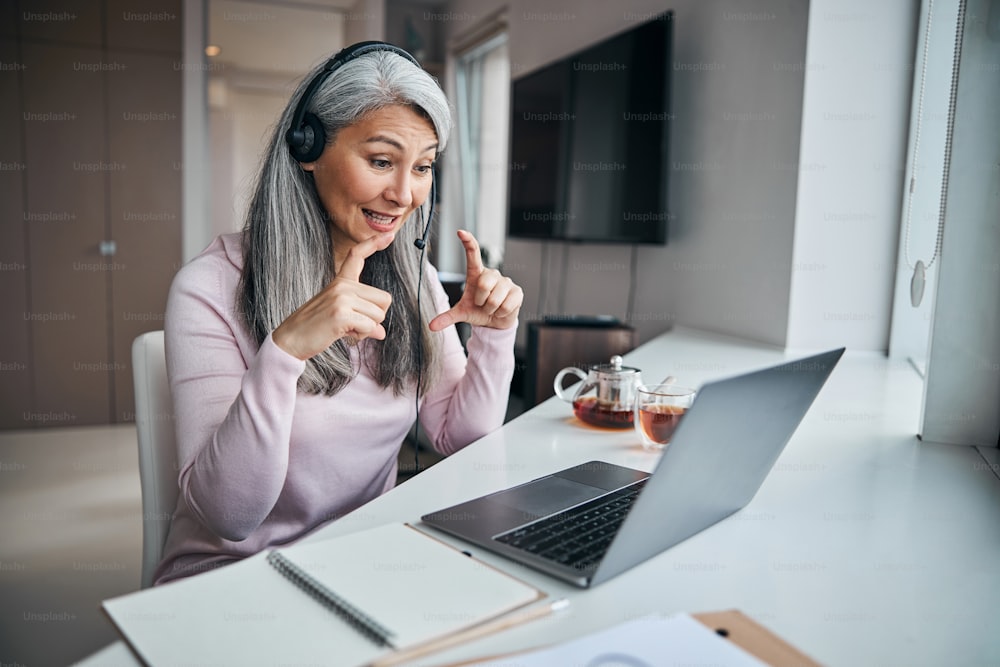 Beautiful lady wearing headset while using modern laptop for online communication at home