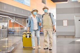 Full-length portrait of a lady with a suitcase and her male spouse staring into the distance