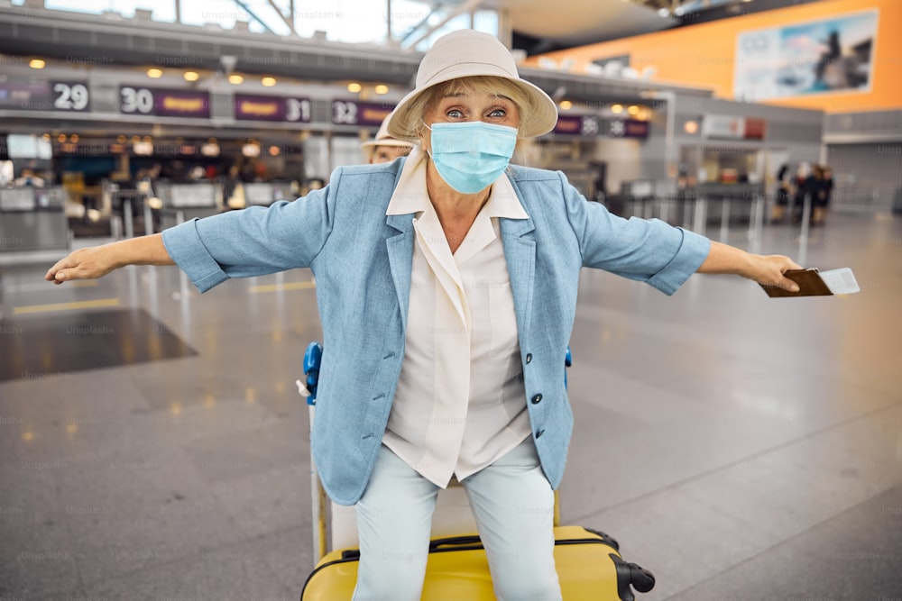 Front view of a cheerful elderly lady tourist enjoying her ride on a baggage trolley