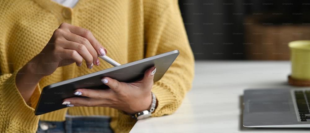 Vista de cerca de una mujer joven que sostiene una tableta digital en la mano y usa un bolígrafo electrónico mientras trabaja en la oficina.