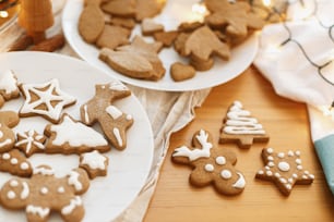 Gingerbread cookies with icing on white plate on wooden table with festive lights. Decorated  christmas tree, star and reindeer cookies with sugar frosting. Christmas holiday tradition and advent