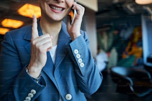 Close up of joyful lady having phone conversation and smiling while pointing index finger up
