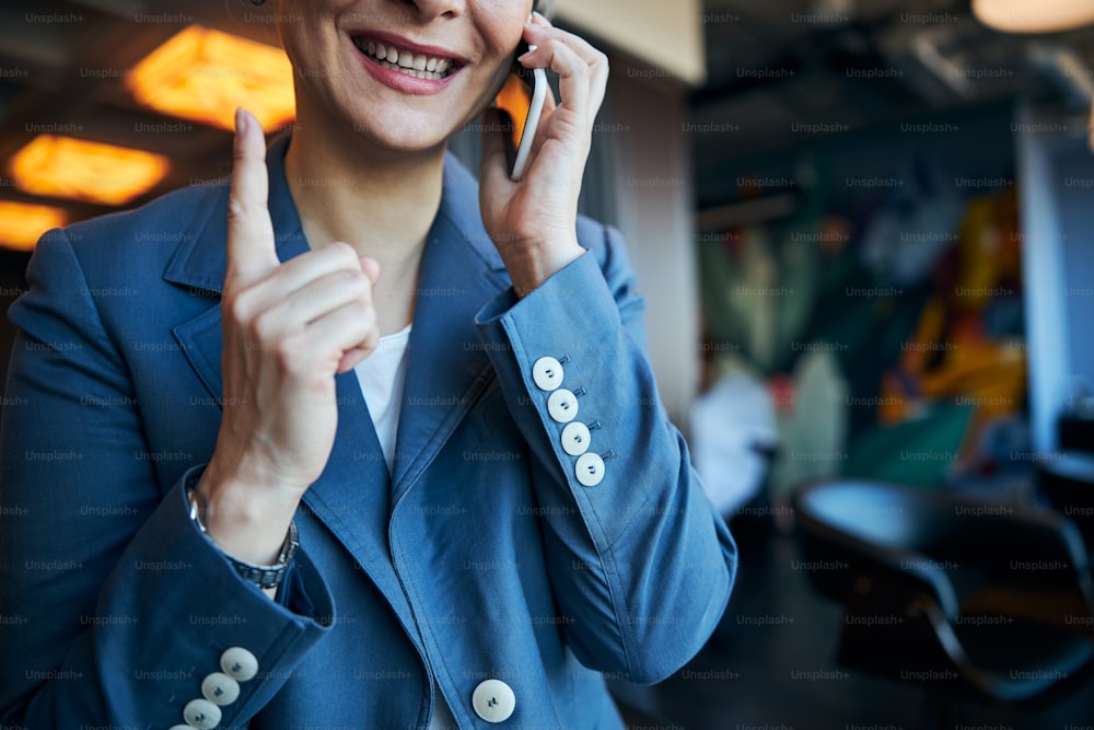 Close up of joyful lady having phone conversation and smiling while pointing index finger up