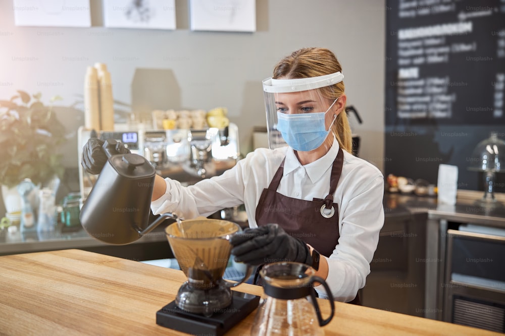 Close up portrait of professional barista preparing coffee using glass coffeemaker pour over coffee maker and drip kettle