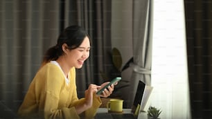 Una joven freelancer está trabajando en su proyecto mientras mira el teléfono inteligente en su habitación.