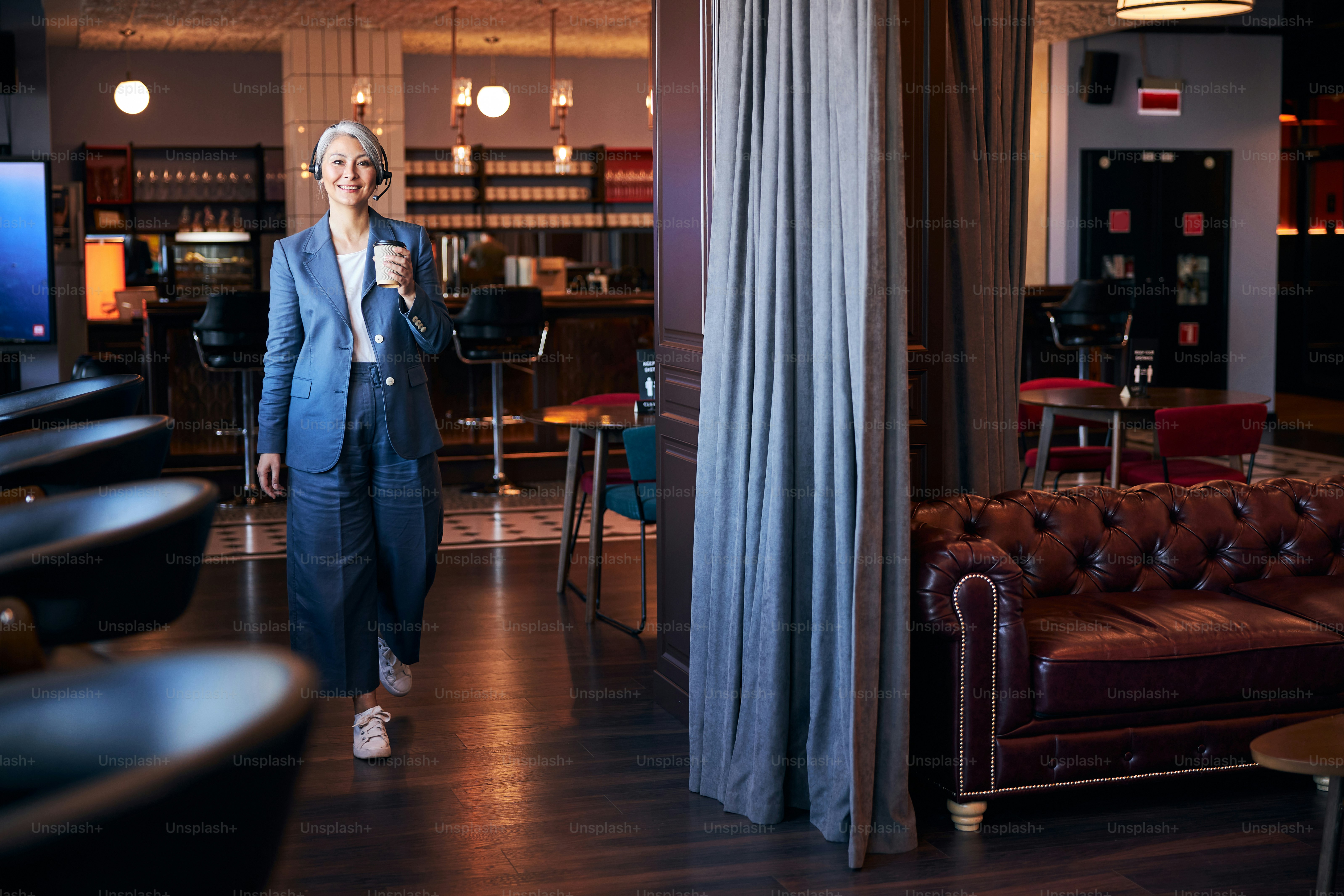 Beautiful lady in elegant suit holding cup of hot drink and smiling while strolling down the cafeteria