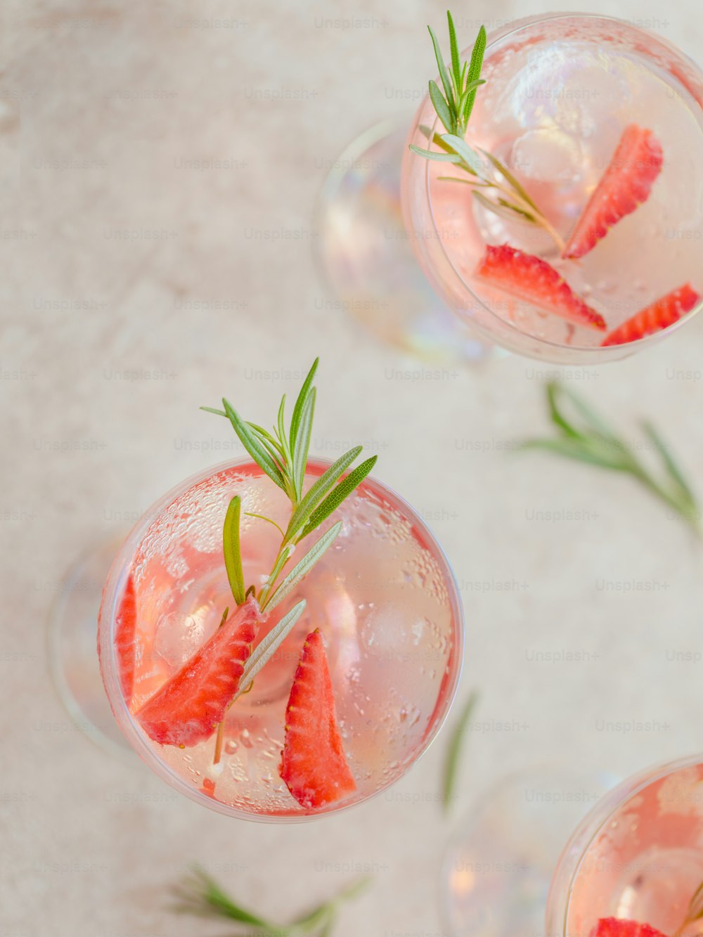Summer drink with white sparkling wine. Homemade refreshing fruit cocktail or punch with champagne, strawberries, ice cubes and rosemary on beige sandy background.