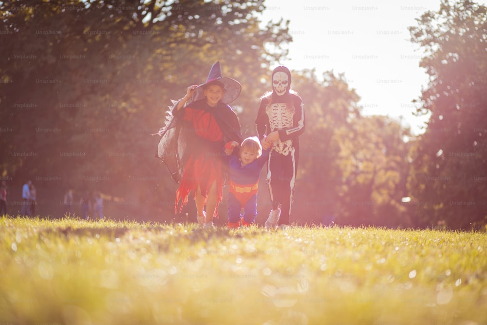 Trois enfants marchant dans la nature dans des costumes d’Halloween.