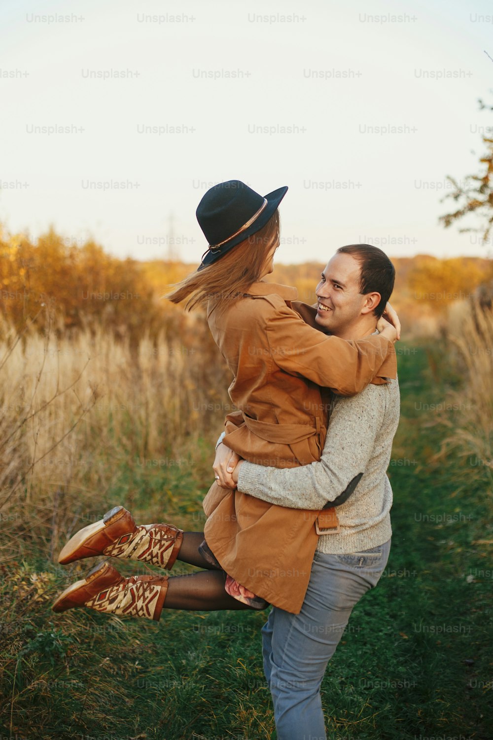 暖かい夕日の光の中で秋の牧草地で踊る幸せなスタイリッシュなカップル。ロマンチックな官能的な瞬間。秋の野原で微笑み、渦巻く若い感情的な女性と男性
