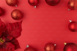 メリークリスマス。赤い背景にポインセチアとクリスマスボールが置かれた平らな横。