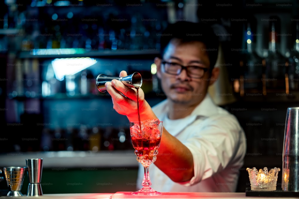 Barista maschio che versa liquore bevanda alcolica in un bicchiere da cocktail misto