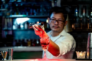Male bartender pouring liquor alcoholic drink into mixed cocktail glass