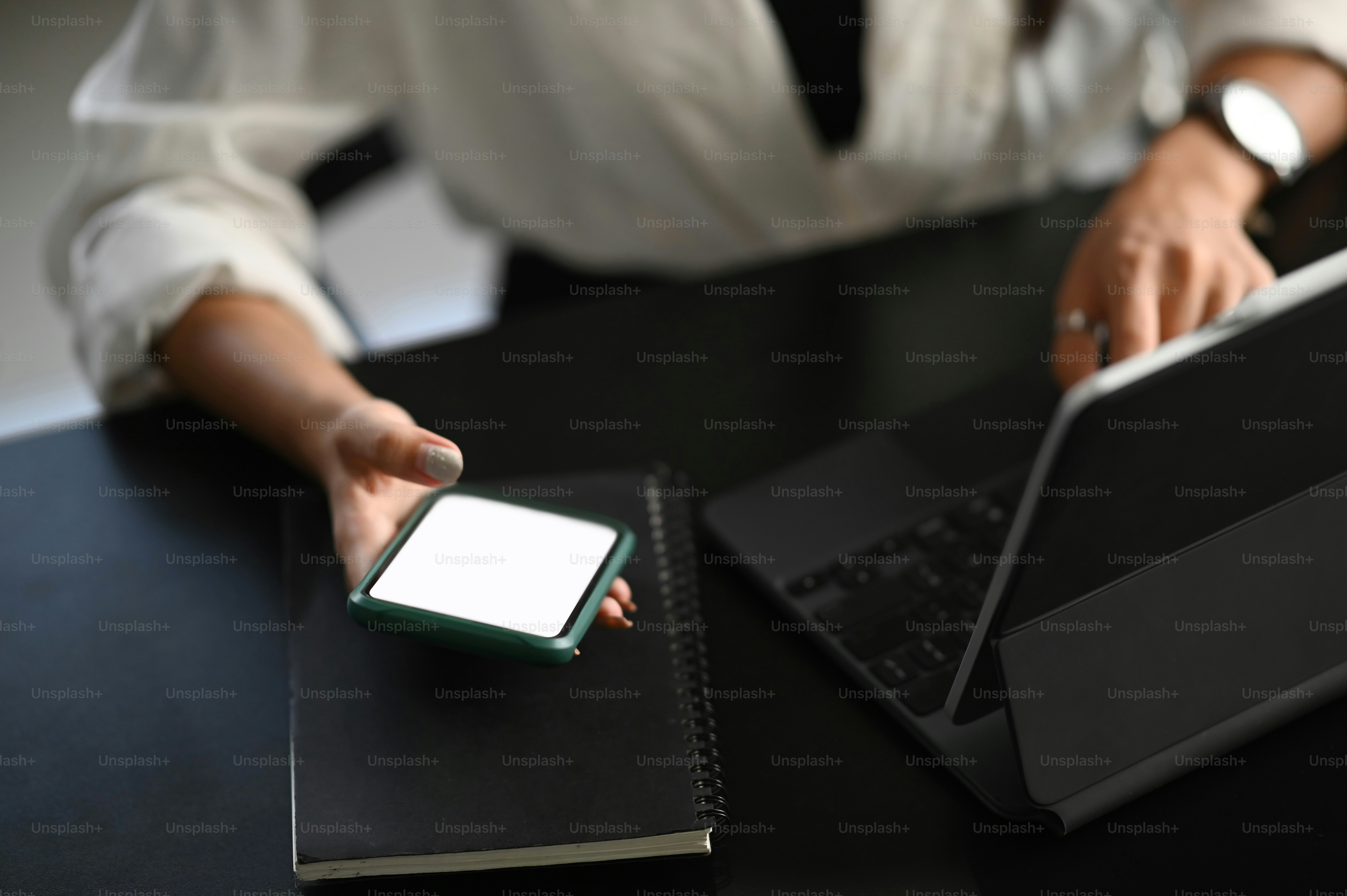 Cropped shot of a young female working on computer laptop in workplace and using blank screen smartphone.
