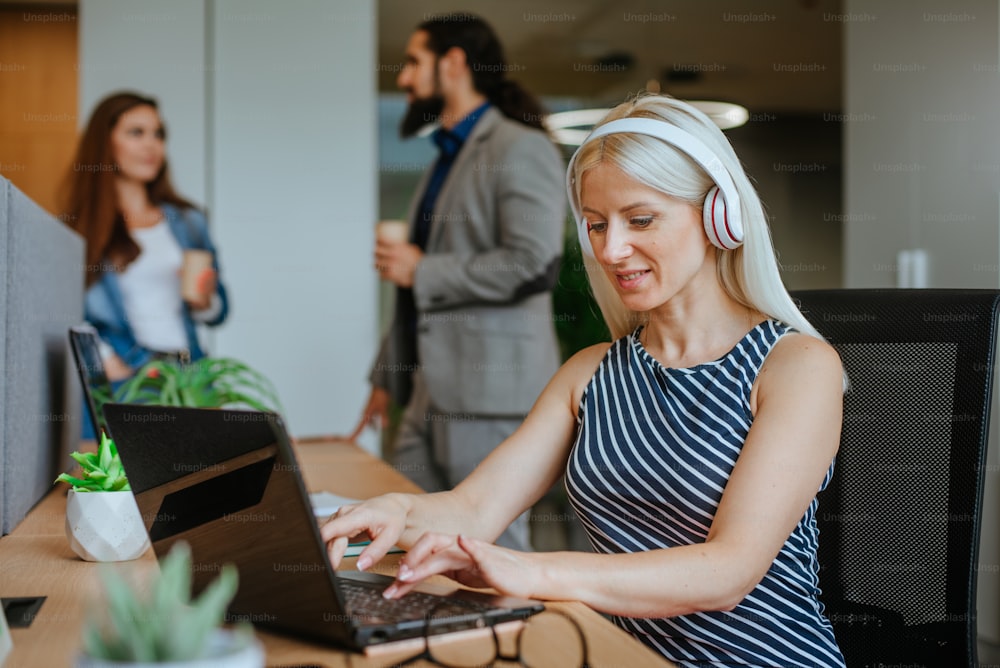 Attractive business woman in the headphones using laptop for work in the modern office.