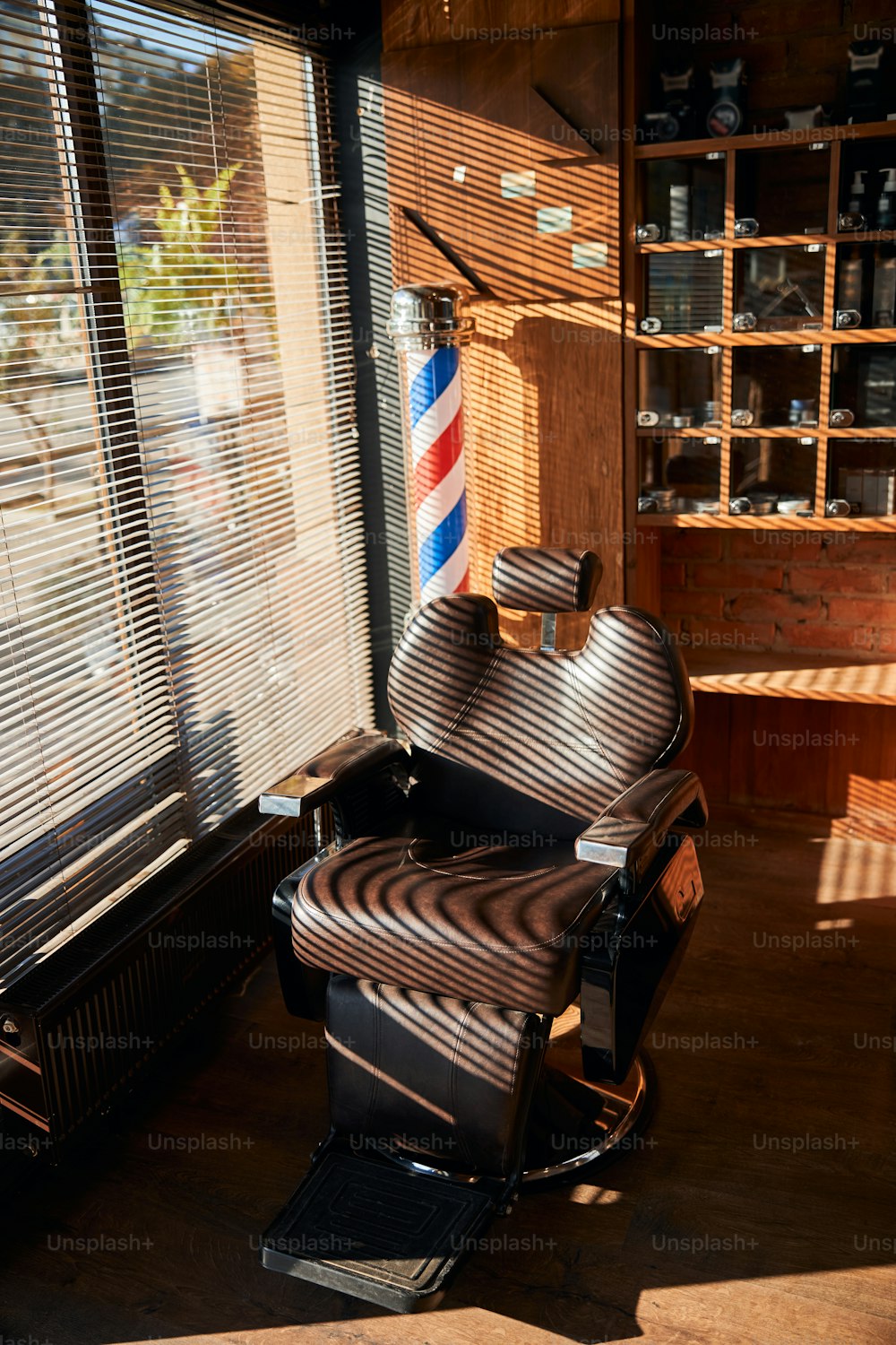 블라인드가 있는 창가에 위치한 조절 가능한 머리 받침이 있는 리클라이닝 갈색 가죽 이발사 의자