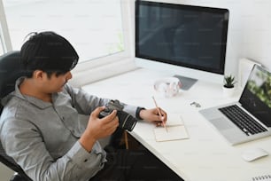 젊은 사진작가가 스튜디오 안의 책상에 앉아 카메라로 캡처한 사진을 검토하고 있습니다.