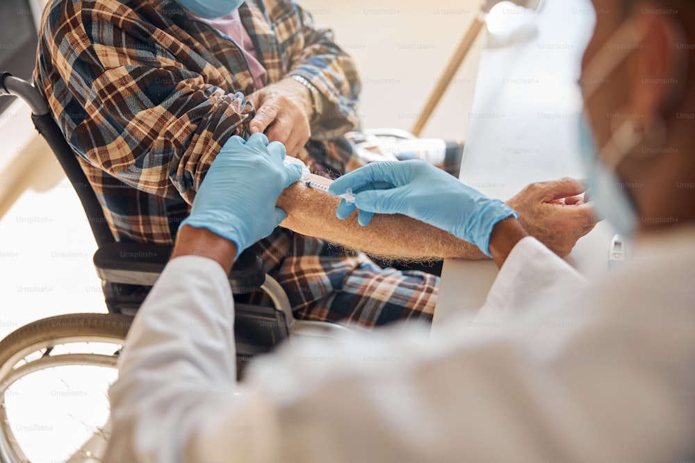 Cropped photo of a healthcare professional administering an injection to an aged Caucasian male pensioner