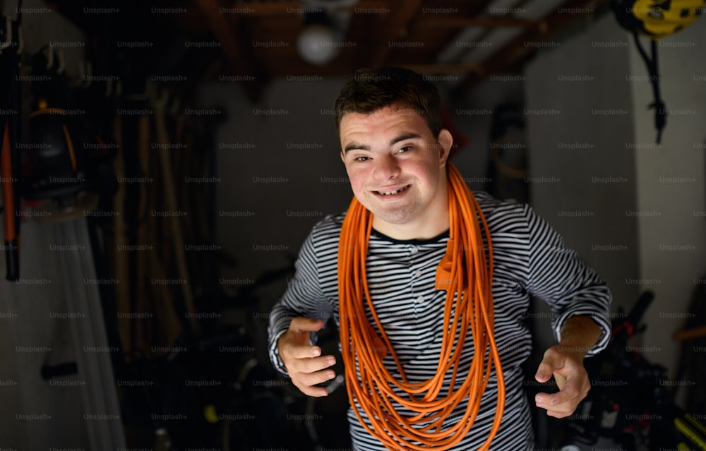 Portrait of down syndrome adult man with rolled up cable around neck in shed looking at camera.