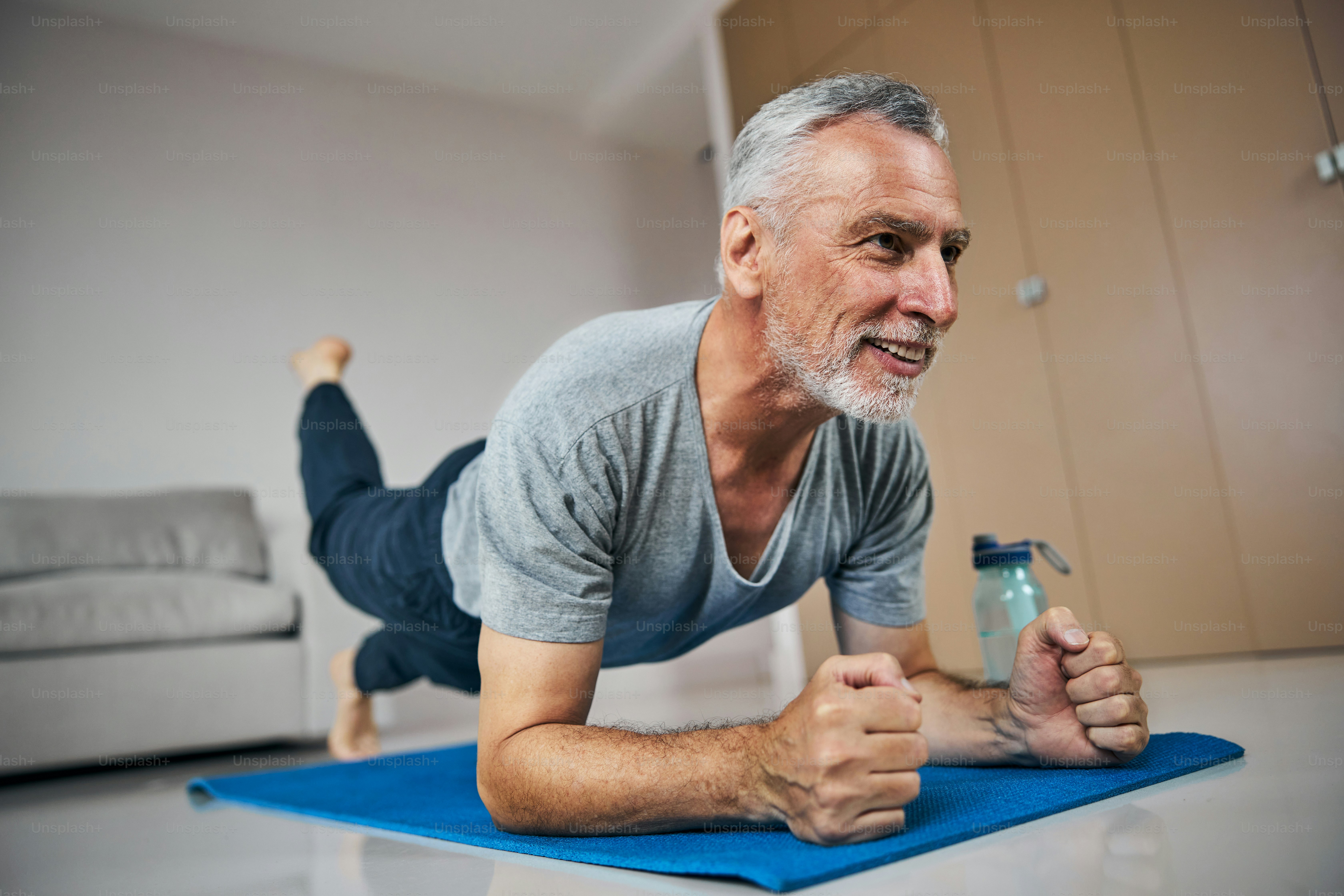 Strong senior citizen doing a plank exercise with lifting one foot off the floor