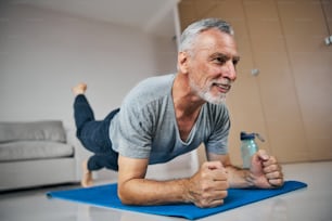 Strong senior citizen doing a plank exercise with lifting one foot off the floor