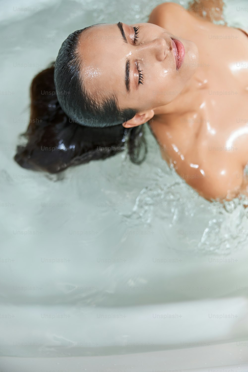 Attractive lady with closed eyes floating in water while taking bath
