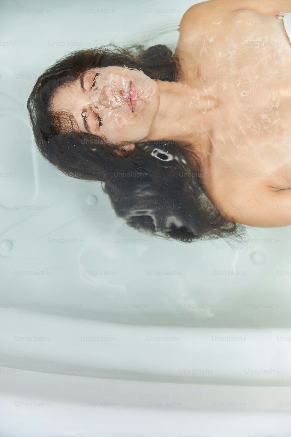 Atractiva dama serena con los ojos cerrados ahogándose en el agua mientras se baña