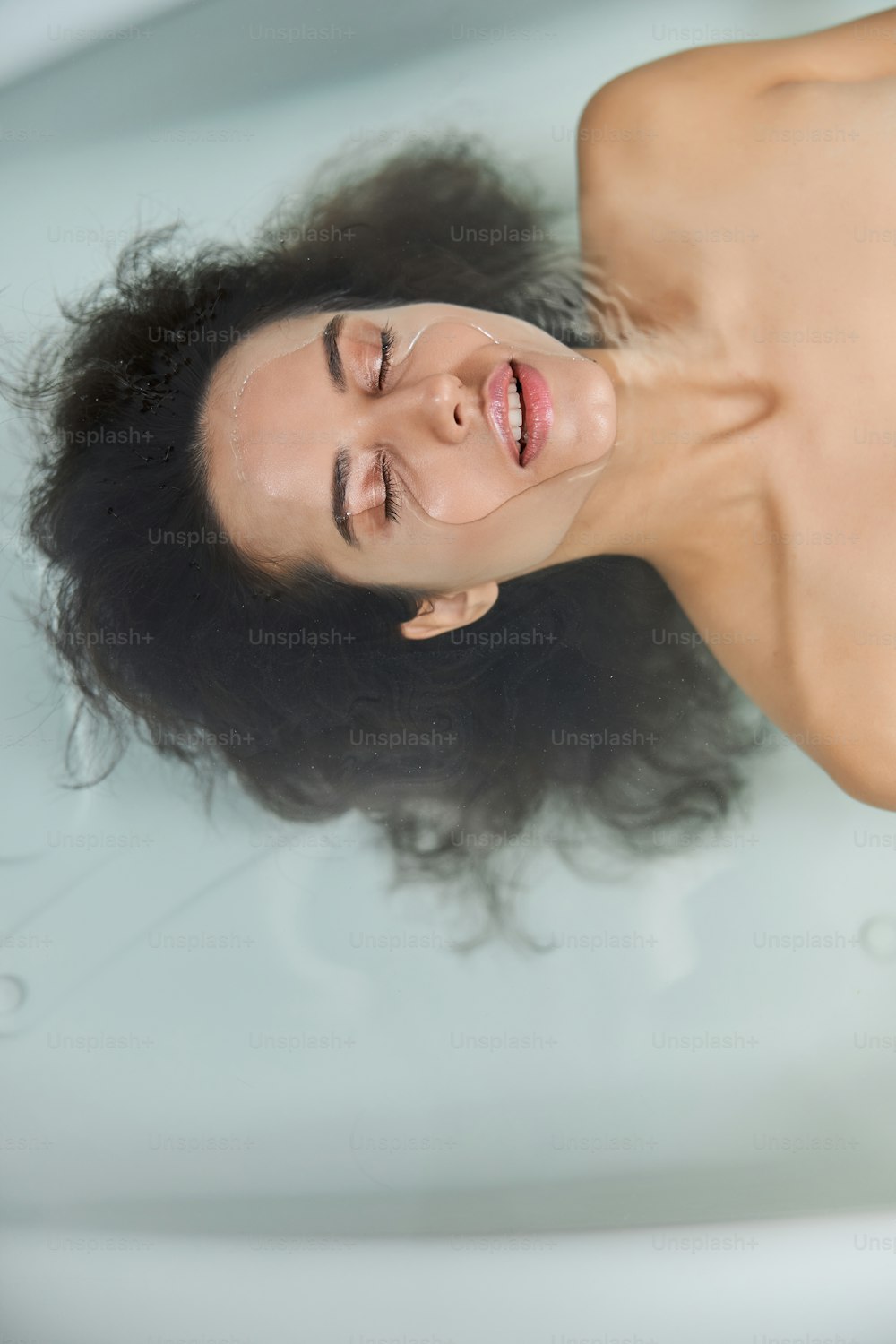 Beautiful serene lady with closed eyes floating in water while taking bath