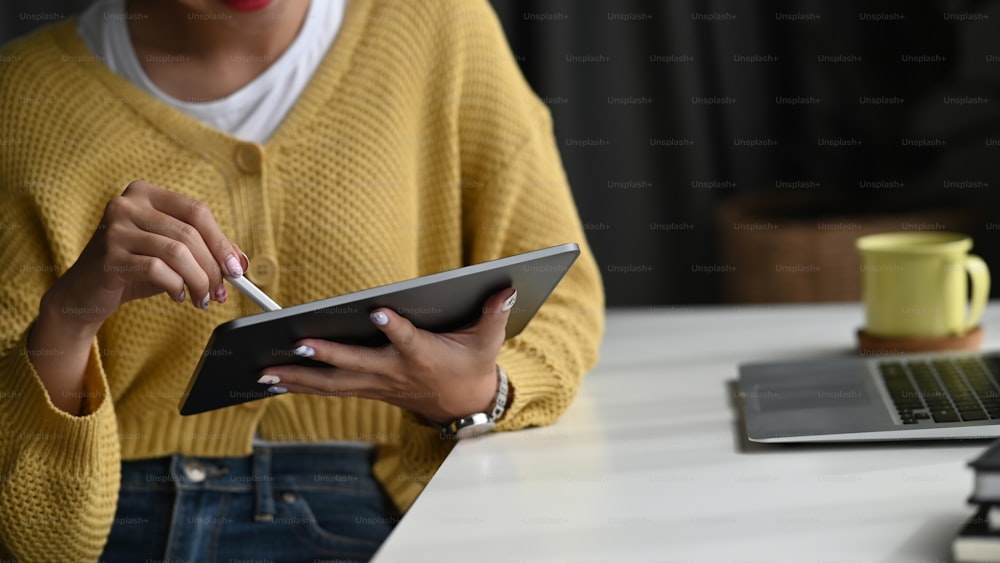 オフィスで仕事をしながらデジタルタブレットを持ち、電子ペンを使用する女性の手の接写。