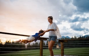Glückliche Mutter mit kleiner Tochter, die auf der Terrasse der Holzhütte spielt, Urlaub in der Natur Konzept.