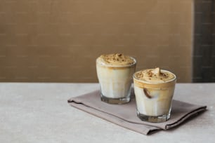 Caffè montato Dalgona, istantaneo, panna, caffè freddo. Cocktail con caffè, latte e cubetti di ghiaccio su sfondo beige chiaro. Sfondo bevanda alla moda con spazio di copia per il testo.