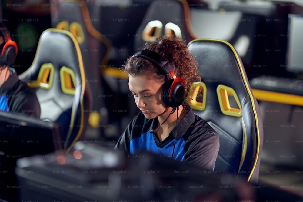 Play to win. Focused teenage mixed race girl, professional female gamer wearing headphones playing online video games, participating in eSports tournament. Online video games
