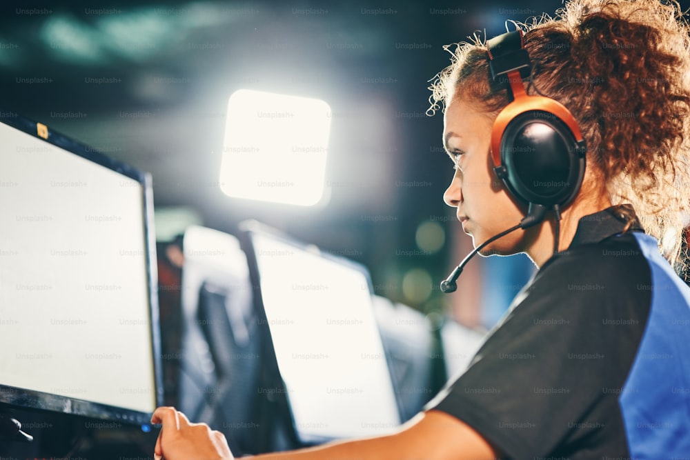 Jugadora de ciberdeportes. Vista lateral de una joven mestiza, totalmente concentrada, con auriculares, jugando videojuegos en línea. Concepto de torneo de eSport
