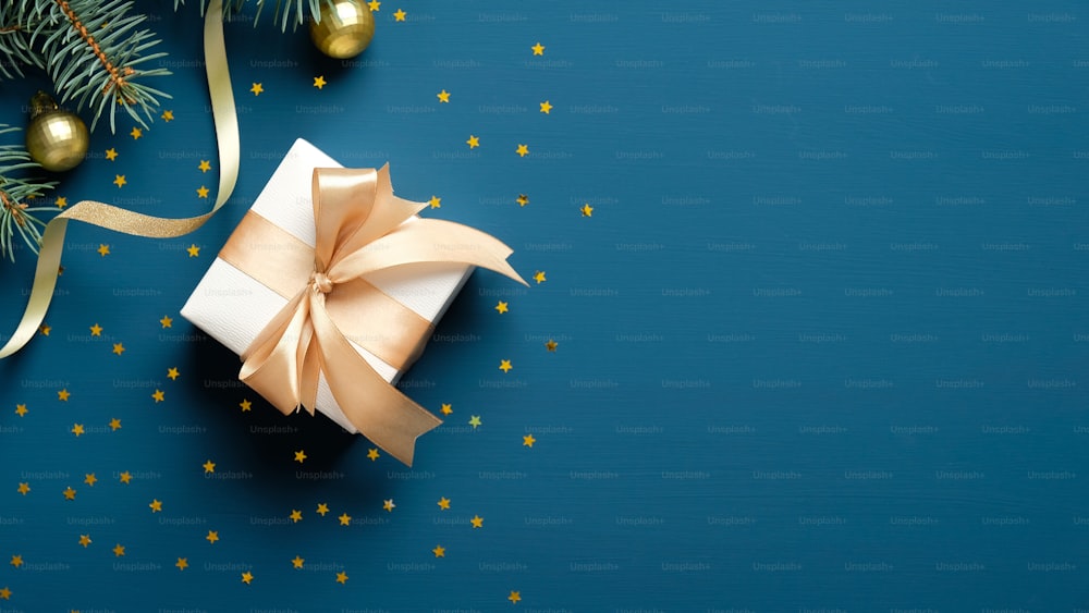 Composizione natalizia. Confezione regalo di Natale, rami di abete, coriandoli dorati su sfondo blu. Posa piatta, vista dall'alto, spazio di copia