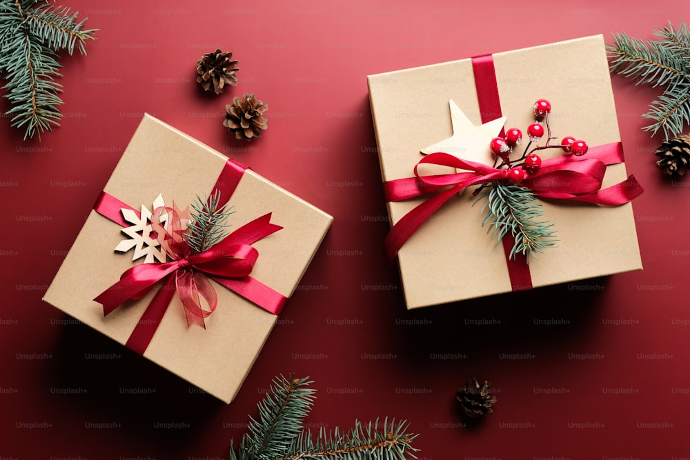 Vintage-Weihnachtsgeschenkboxen verzierten rote Bandschleife und Tannenzweige auf marsalarotem Hintergrund. Weihnachtsgeschenk-Konzept.