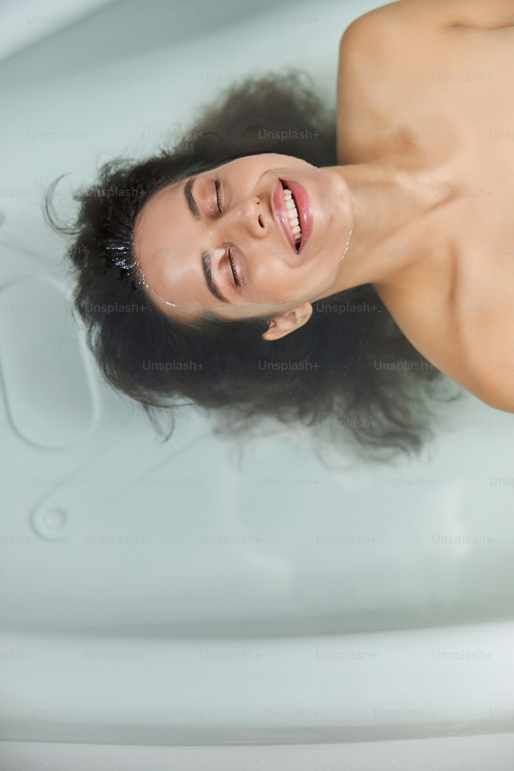 Beautiful lady with closed eyes floating in water and smiling while taking bath