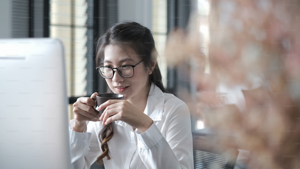 Young confident female business worker is sitting in office and drinking coffee ready for the work day.