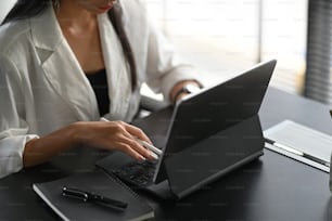 Cropped shot of young female holding stylus pen while working on computer tablet at her workspace.