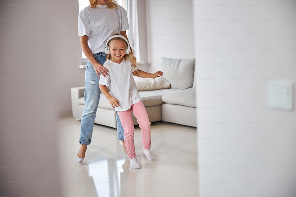 Retrato de cerca de una niña pequeña sonriente feliz bailando con mamá en la sala de estar grande en el fin de semana